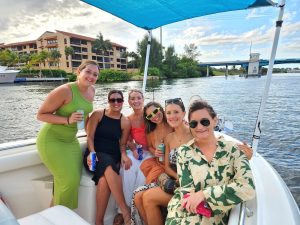 A group of girl friends on a boat ride posing for a group photo on the bow of a boat during a custom boat charter