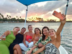 A group of dressed up girlfriends taking a selfie together with a sunset view in the background during a 3 hour sightseeing boat tour