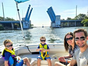 A family with children out on the water enjoying a family boat charter with an open drawbridge in the distance