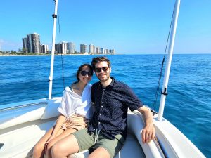 A couple pose for a photo on a boat out on the Atlantic Ocean with the coast of Singer Island in the distance