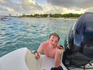 Boy climbing into back of boat from water holding a seashell
