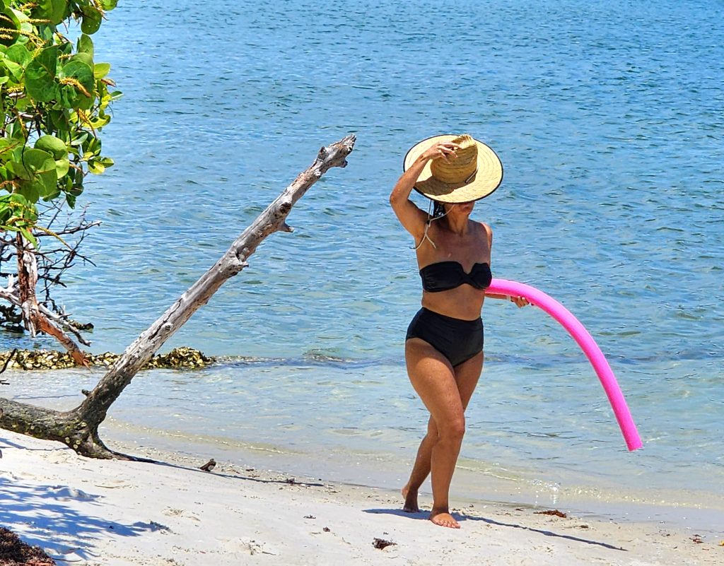 Lady in swim wear and a sunhat walking the beach alone carrying a pool float