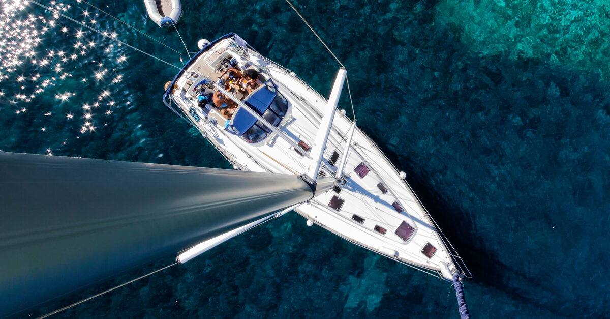 An aerial view of a sailboat charter ship near the sandbar pulling a small inflatable raft behind it.
