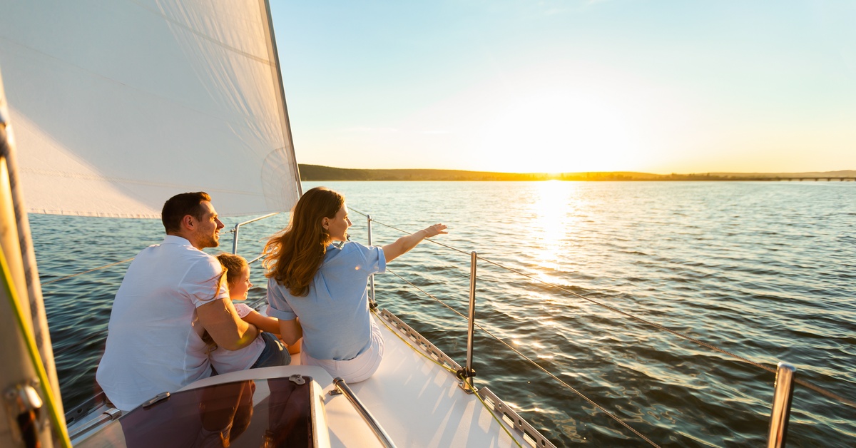 A husband, wife, and child are all sitting at the front of a private yacht. The mother is pointing out at sea.