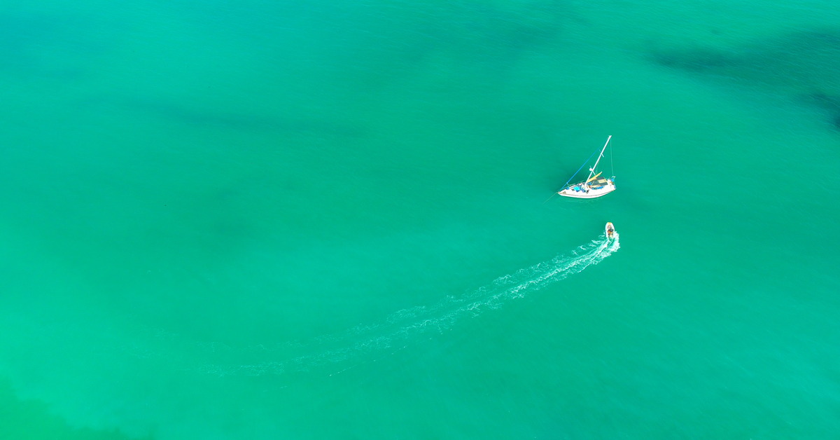 An open body of water with two boats in it. The smaller boat is going toward the larger one to dock.