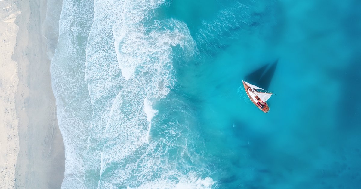 An aerial view of a yacht cruising in the ocean. They're near the shoreline of the sea, preparing for docking.