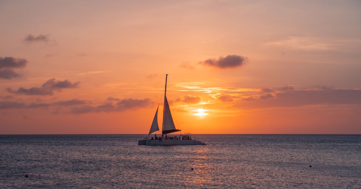 A sunset cruise is silhouetted by the setting sun on the open sea. There are many people on the boat.