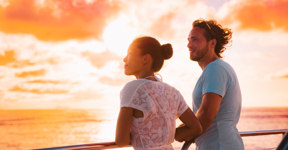 A close-up of a couple looking out onto the ocean on a sunset cruise. The sun is shining on their faces.