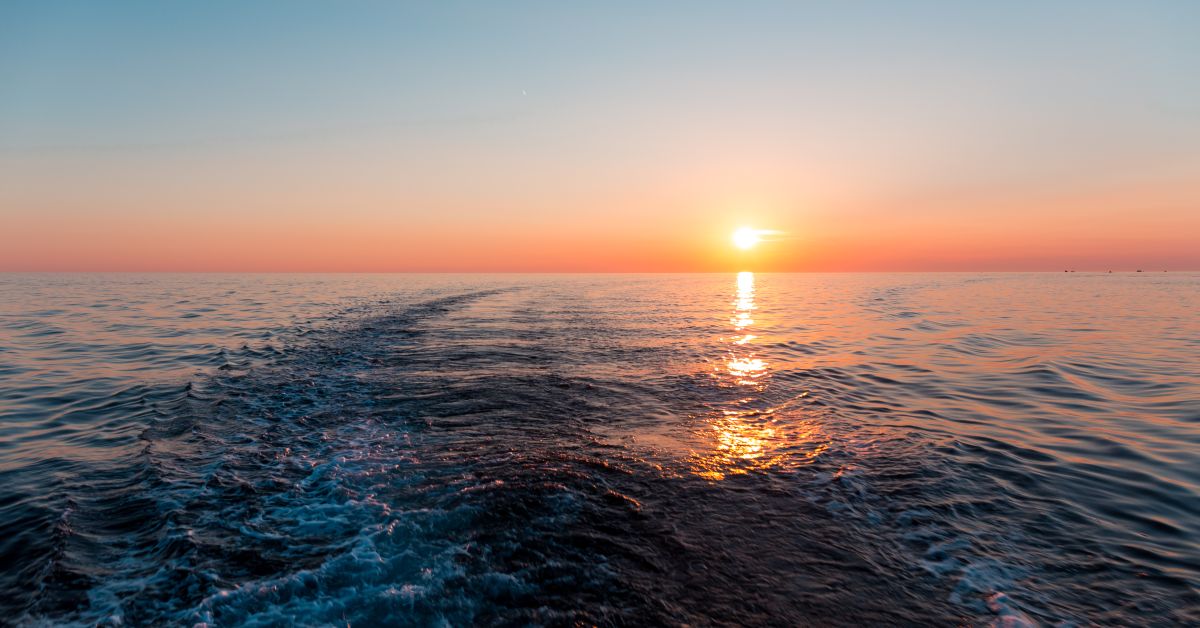 A close-up of the ocean as the sun sets. The sky is blue, orange, and pink, and it is reflected in the water.